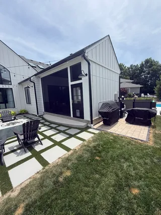 Screened porch with black trim on white farmhouse above paver and turf patio