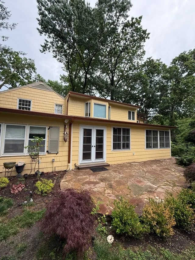 Sunroom addition with window walls on yellow home above flagstone patio